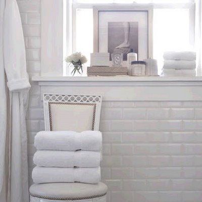 white bathroom with white subway tile and a stack of white towels folded in a chair